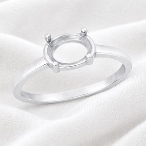 May include: A polished silver-toned ring setting featuring a circular head with four prongs designed to hold a gemstone. The band is smooth and solid, showcasing a clean, metallic finish that reflects light across its curved, rounded surface.