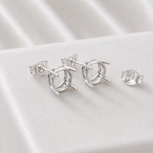 May include: A pair of sterling silver earring settings with four prongs designed for holding round gemstones. Each earring post features a 925 stamp, and a matching 925 stamped earring back is included for secure fastening of the jewelry components.