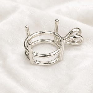 May include: A silver-toned metal pendant setting featuring a circular frame with four vertical prongs designed to hold a gemstone. The setting includes a small, looped bail attached to the side for hanging on a chain or cord, with a polished finish.