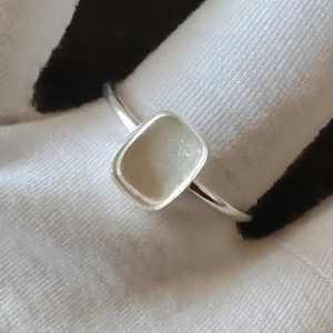 May include: A silver ring featuring a smooth, polished band and a square-shaped bezel setting with rounded corners. The setting is currently empty, showcasing a recessed, reflective metallic interior surface within the square frame.