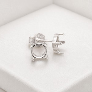 May include: A pair of sterling silver stud earring settings featuring a four-prong basket design for holding a round gemstone. The earring backs are clearly stamped with the number 925, indicating the silver content of the metal components.