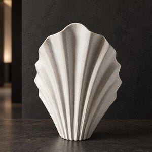 May include: A light gray, fan-shaped vase with a textured, matte finish. The object features a series of vertical, radiating ridges that mimic the appearance of a large seashell, tapering down to a narrow, flat base for stability.