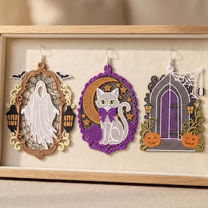 Puede incluir: Tres adornos colgantes bordados con motivos de Halloween. El de la izquierda muestra un fantasma blanco en un marco marrón con murciélagos. El central presenta un gato blanco con un lazo morado y una luna creciente. El derecho muestra una puerta morada con calabazas.