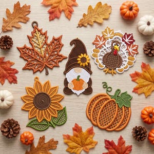 Può includere: Una collezione di cinque ornamenti ricamati a tema autunnale che include una foglia d'acero, uno gnomo con una zucca, un tacchino, un girasole e una zucca, circondati da foglie di quercia essiccate, pigne e piccole zucche decorative.