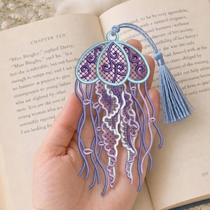 May include: A jellyfish-shaped bookmark crafted from intricate purple and light blue embroidery thread. The design features a rounded top with a lattice pattern, dangling tentacles, and a matching light blue tassel attached to a small loop at the top.