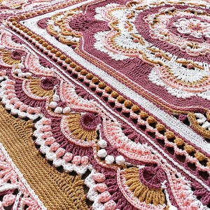 Könnte beinhalten: Eine gehäkelte Decke mit einem komplexen, von Mandalas inspirierten Muster in den Farben Altrosa, zartem Rosa, Weiß und Senfgelb. Das Design umfasst aufwendige Maschenarbeiten, darunter Muschelmuster, Noppenstiche und strukturierte Ränder.