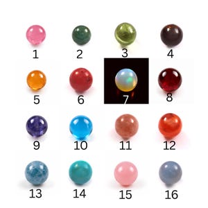 May include: A collection of sixteen spherical beads arranged in a four-by-four grid, each labelled with a number from 1 to 16. The beads display a variety of colours including pink, green, orange, red, blue, purple, and an iridescent white opal-like bead.