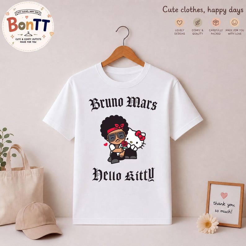 May include: White t-shirt featuring a graphic of Bruno Mars and Hello Kitty. The design includes the text "Bruno Mars" above the illustration and "Hello Kitty" below. The shirt is hanging on a wooden hanger.