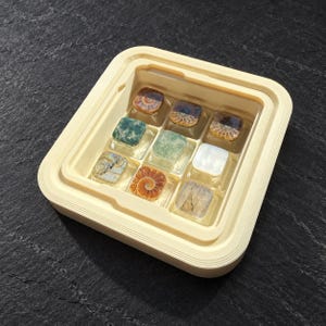 May include: A square, cream-coloured plastic tray containing nine individual square keycaps arranged in a three-by-three grid. Each keycap features a unique embedded design, including fossilised ammonite spirals, green stone textures, and a white pearlescent finish.