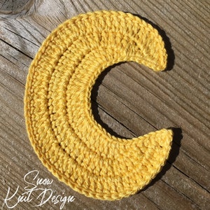 May include: A yellow crocheted crescent moon shape.