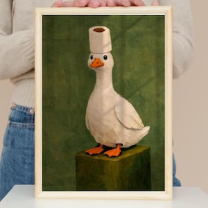 Può includere: Una stampa artistica incorniciata raffigurante un'anatra bianca con becco e zampe arancioni in piedi su un blocco verde scuro. L'anatra ha un rotolo di carta igienica bianca in equilibrio sulla testa su uno sfondo verde scuro testurizzato.