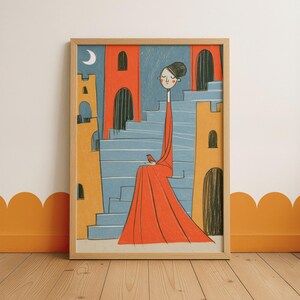 Könnte beinhalten: Ein gerahmter Kunstdruck mit einer stilisierten Illustration einer Figur in einem langen roten Kleid, die auf einer blauen Treppe sitzt. Die Szene zeigt orangefarbene und gelbe schlossartige Gebäude, einen kleinen roten Vogel und einen weißen Mond.