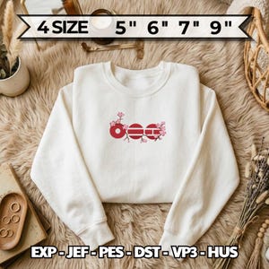 May include: A white sweatshirt with a crew neck features a red floral design with the word "OEE" in a stylized font. The sizes are 5", 6", 7", and 9". The sweatshirt is displayed on a textured surface.