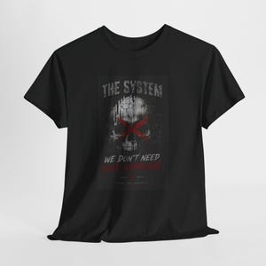 Può includere: T-shirt nero con grafica a teschio invecchiata e 'X' rossa. Il testo recita "THE SYSTEM" e "WE DON'T NEED YOUR APPROVAL". La maglietta è realizzata in materiale morbido. Un design per chi vuole fare una dichiarazione.