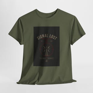 May include: Olive green t-shirt featuring a black rectangle with the words "SIGNAL LOST" in a vintage font. A red circle surrounds a radio tower graphic. The text "DISCONNECT. RECONNECT." is below the graphic. The shirt is made of a soft material.