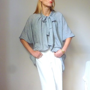 May include: A gray, loose-fitting blouse with a bow tie at the neck. The blouse has short sleeves and a relaxed fit.