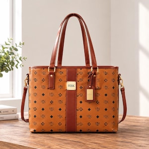 May include: A tan tote bag featuring a repeating black monogram pattern and the letters HBK. The bag has brown leather-like handles, a vertical brown center stripe, and a gold-toned metal plaque on the front center engraved with the letters HBK.