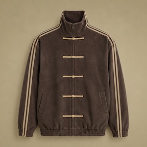 May include: A dark brown zip-up track jacket featuring a high collar, long sleeves with dual beige stripes, and a front closure with four beige toggle-style frog fasteners. The jacket includes ribbed cuffs and a ribbed hem at the bottom edge.