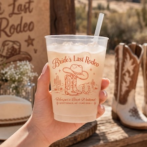 May include: A clear plastic cup filled with ice and a straw, featuring orange printed text that reads Bride's Last Rodeo, Harper's Bach Weekend, and SCOTTSDALE, AZ • JUNE 2026, alongside illustrations of a cowboy hat, boots, cacti, and a horseshoe.