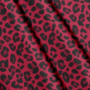 Könnte beinhalten: Ein Stoff mit einem sich wiederholenden Leopardenmuster mit schwarzen Flecken auf einem tiefroten Hintergrund. Das Material weist eine sichtbare Webstruktur mit weichen Falten auf, die diagonal über die Oberfläche verlaufen.