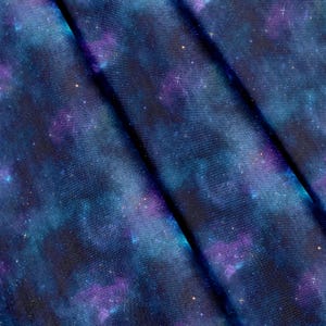 Könnte beinhalten: Ein Stoff mit einem Weltraum-Druck, der wirbelnde Wolken in Dunkelblau, Marineblau und Violett zeigt. Das Muster ist mit verstreuten, sternartigen weißen Punkten unterschiedlicher Größe akzentuiert, was dem gefalteten Material eine Textur verleiht.