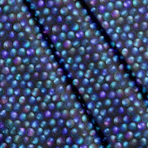 Op de afbeelding: Een stof met een herhalend patroon van cirkelvormige figuren in tinten diepblauw, paars en groenblauw. De cirkels hebben een metallic, iriserende afwerking die een gevoel van diepte en textuur creëert over het oppervlak van het materiaal.
