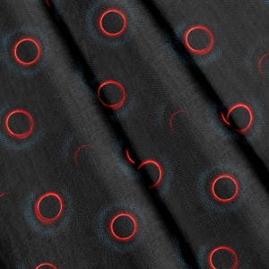 Op de afbeelding: Een zwarte stof met een herhalend patroon van levendige rode cirkelvormige contouren. Elke rode ring is omgeven door een subtiele, donkergrijze gestippelde halo, wat een textuur creëert over het oppervlak van het gevouwen materiaal.