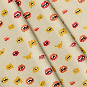 Op de afbeelding: Een beige stof met een herhalend patroon van kleine gele monsters met scherpe tanden en rode lippen met witte tanden. Het ontwerp is over het oppervlak van het textiel gedrukt en toont een consistente rangschikking van deze grafische elementen.