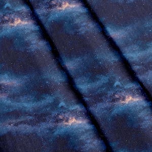 Könnte beinhalten: Ein Stoff mit einem Weltraum-Motiv in tiefem Marineblau und Schwarz, übersät mit weißen Punkten, die Sterne darstellen, sowie weichen, verblendeten hellblauen und orangefarbenen Bereichen, die an eine ferne Galaxie oder einen Nebel erinnern.