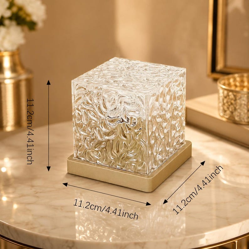 May include: A clear, cube-shaped glass lamp with a textured, rippled surface, set on a square gold-toned base. The lamp measures 11.2 cm or 4.41 inches in height, width, and depth, as indicated by the visible measurement labels.