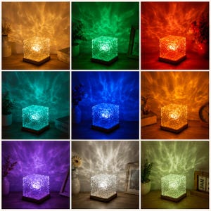 May include: A square glass lamp with a textured, rippled surface that projects colorful light patterns onto the surrounding wall. The lamp sits on a flat wooden base and is shown in nine different color variations including orange, green, red, teal, blue, yellow, purple, white, and light green.