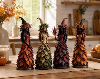 May include: Four standing witch figurines wearing pointed hats and dresses crafted from layered autumn leaves in shades of orange, yellow, red, and brown. Each figure features dark hair and holds a small accessory, displayed on a wooden table.