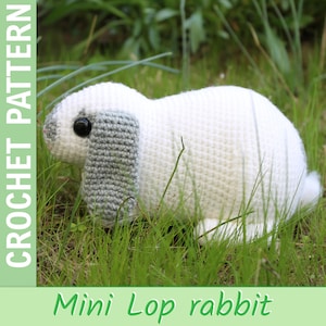 Könnte beinhalten: Ein weißer Mini-Lop-Häschen-Häkelarbeit mit grauen Ohren und einem schwarzen Auge, das im grünen Gras sitzt. Das Bild enthält den Text "CROCHET PATTERN" und "Mini Lop rabbit" in Grün.
