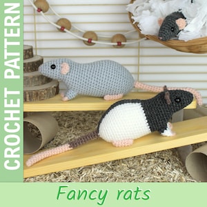 Puede incluir: Ratas de fantasía de ganchillo en gris, negro y blanco, con detalles en rosa. La imagen incluye el texto "CROCHET PATTERN" y "Fancy rats". Las ratas se muestran en una estantería de madera con un entorno similar a una jaula.