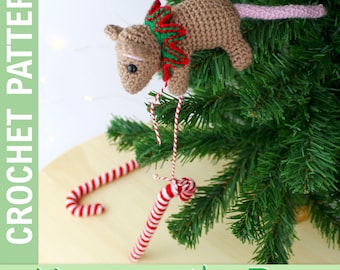 May include: A crocheted mouse Christmas ornament with a red and green scarf, hanging on a green Christmas tree. The mouse has a pink tail and is near a red and white candy cane. Text reads "CROCHET PATTERN" and "Mouse on the Tree".