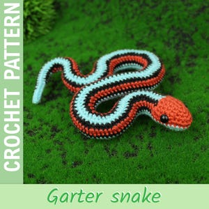 Könnte beinhalten: Gehäkelte Strumpfbandnatter in Rot, Schwarz und Hellblau, mit rotem Kopf und schwarzen Augen. Der Text "CROCHET PATTERN" befindet sich auf der linken Seite und "Garter snake" unten.