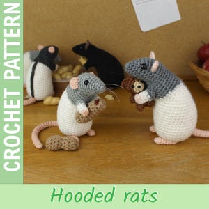 Puede incluir: Patrón de crochet para ratas con capucha. La imagen muestra varias ratas amigurumi hechas a mano en diferentes poses. Las ratas son principalmente blancas, grises y negras, con orejas y colas rosas. Algunas ratas sostienen cacahuetes o un pequeño osito de peluche. El texto "CROCHET PATTERN" y "Hooded rats" son visibles.