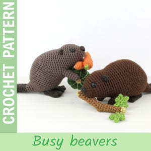 Könnte beinhalten: Zwei gehäkelte Biber, einer hält ein grünes und orangefarbenes Gemüse, der andere einen braunen Stock und grüne Blätter. Der Text "CROCHET PATTERN" steht links und "Busy beavers" unten.