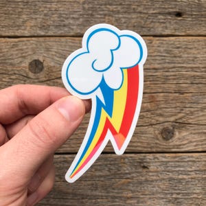 May include: A die-cut vinyl sticker featuring a white cloud with a stylized rainbow lightning bolt extending downward. The lightning bolt design incorporates vibrant bands of blue, yellow, and red colors with a clean white border outline.