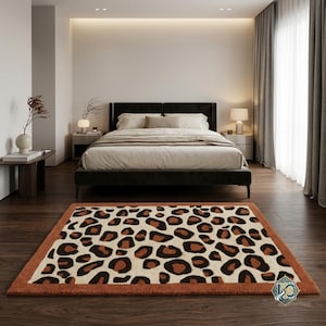 Puede incluir: Una alfombra rectangular con un llamativo estampado de leopardo con manchas de color marrón oscuro y negro sobre un fondo crema, enmarcada por un borde sólido de color naranja quemado. La alfombra se sitúa sobre un suelo de madera oscura.