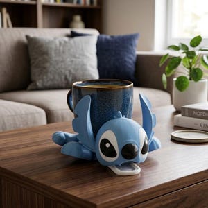May include: A blue ceramic mug with a gold rim rests in a light blue Stitch-shaped holder on a wooden coffee table. The mug is filled with a dark liquid. Decorative plants and books are in the background.