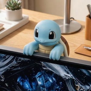 May include: A light blue turtle-like character figure with a brown shell, large dark eyes, and a smooth finish, designed to hang over the top edge of a computer monitor. The figure features rounded limbs and a small tail visible on the back.