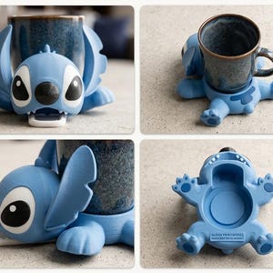 May include: A light blue 3D-printed Stitch-shaped mug holder. The holder has large black eyes, a black nose, and open mouth. The holder is designed to cradle a mug. The base of the holder has the text "ALOHA PRINTWORKS HANDCRAFTED IN HAWAII".