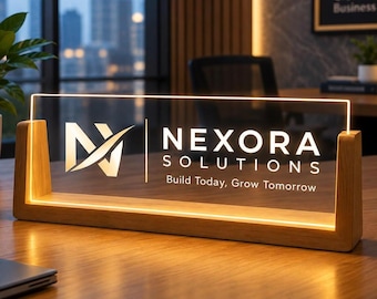 May include: A rectangular clear acrylic sign with a light-up edge, held by a wooden base. The sign features the white logo and text Nexora Solutions Build Today, Grow Tomorrow. The light emits a warm glow along the bottom and sides.