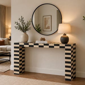 Peut inclure: Une console rectangulaire au motif à damier noir et beige. Le plateau est décoré d'un vase en céramique contenant du feuillage vert, de deux livres empilés et d'une lampe de table sombre et côtelée avec un abat-jour en tissu beige.