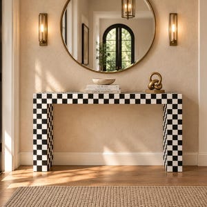 May include: A rectangular console table featuring a black and white checkered pattern across its entire surface. The table has two thick, block-style legs and a flat top surface, providing a stable structure for displaying decorative items.