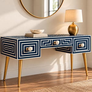 May include: A rectangular console table featuring a deep navy blue finish with white geometric Greek key patterns. The piece includes three drawers with white floral-shaped knobs and is supported by four tapered gold-toned metal legs.