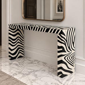 May include: A rectangular console table featuring a bold black and white zebra stripe pattern. The table has a flat top surface and two vertical side panels that extend to the floor, creating a continuous, seamless look across the entire structure.