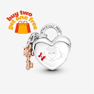 May include: A silver heart-shaped padlock charm featuring the engraved text A PERFECT PAIR, a white enamel hand gesture design, and a small red bow. Attached to the padlock is a rose gold-toned key charm with a detailed, ornate handle design.