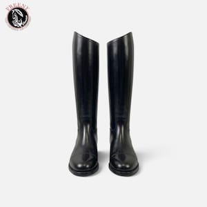 Puede incluir: Un par de botas de montar altas de color negro con acabado liso, punteras redondeadas y caña exterior alta. Las botas presentan un diseño limpio con una silueta estructurada y un logotipo en la esquina superior que dice FREENY.
